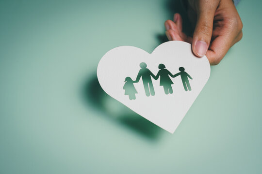 Hand lifting heart cutout with family silhouettes, emotional support awareness, relationship stability, mental wellbeing reflection, family care protection, unity bonding concept