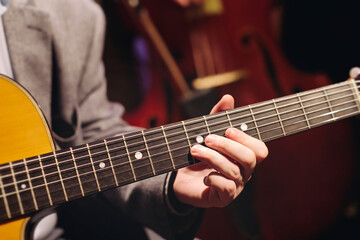 Fototapeta premium Concert view of acoustic electric guitar player with vocalist and rock band performing in a club, male musician guitarist on stage with audience in a crowded concert club hall arena, hands on guitar