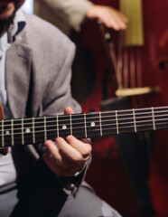 Obraz premium Concert view of acoustic electric guitar player with vocalist and rock band performing in a club, male musician guitarist on stage with audience in a crowded concert club hall arena, hands on guitar