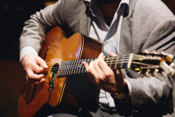 Concert view of acoustic electric guitar player with vocalist and rock band performing in a club, male musician guitarist on stage with audience in a crowded concert club hall arena, hands on guitar