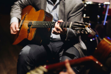 Obraz premium Concert view of acoustic electric guitar player with vocalist and rock band performing in a club, male musician guitarist on stage with audience in a crowded concert club hall arena, hands on guitar