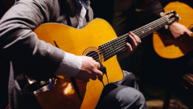 Concert view of acoustic electric guitar player with vocalist and rock band performing in a club, male musician guitarist on stage with audience in a crowded concert club hall arena, hands on guitar - Powered by Adobe
