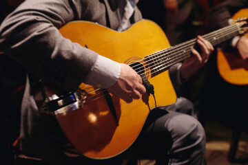 Obraz premium Concert view of acoustic electric guitar player with vocalist and rock band performing in a club, male musician guitarist on stage with audience in a crowded concert club hall arena, hands on guitar