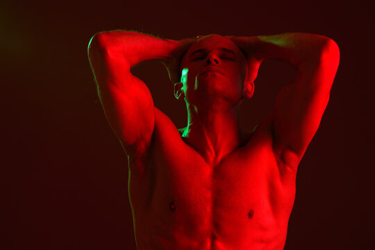 Strong man posing with hands on head, showcasing defined muscles and a dramatic red light effect, creating a striking atmosphere. Perfect for fitness and wellness themes.