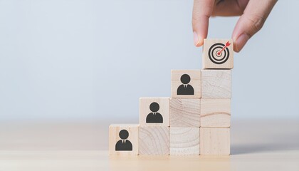 Hand places target icon on top of wooden blocks with people icons, symbolizing career growth and goal achievement.