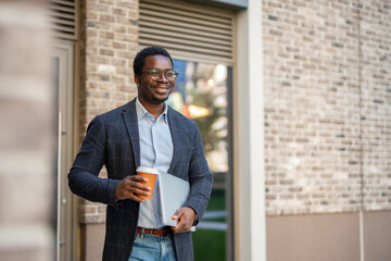 Smiling young man walking with coffee and laptop