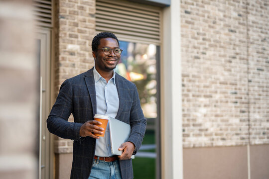 Smiling young man walking with coffee and laptop