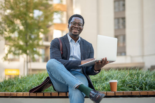 Happy black man working on laptop outdoors - Powered by Adobe