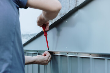 Young worker installs roofing on metal shed with screwdriver.