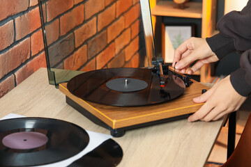 Woman turning record player with vinyl disk on at home, closeup