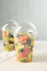 Tasty fruit salad in plastic cups on beige table, closeup