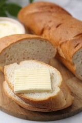 Cut baguette with butter on white table, closeup