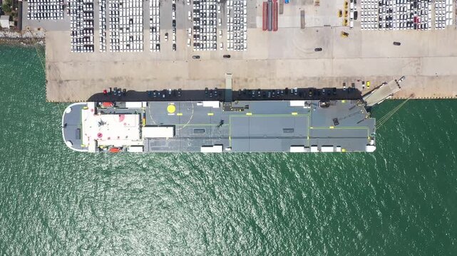 Roro ship top view in export and import business and logistics. Shipping cargo to harbor. Aerial view of a large number of new cars lined up outside an automobile factory ready to ship over sea.