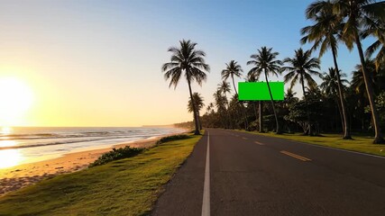 Empty coastal road alongside a tropical beach during a beautiful sunrise, featuring a blank green screen billboard for advertising mockups