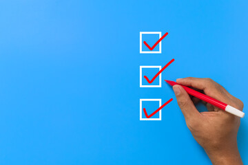 close up of male hand holding red marker and checklist three checkbox isolated on blue background