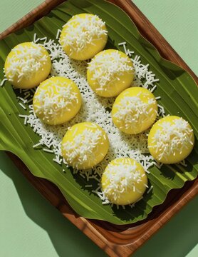 Sweet yellow rice cake coconut topping banana leaf on wooden tray, fresh tropical dessert snack, round minimal style overhead shot