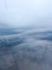 A serene aerial view of winding rivers and fields partly veiled by soft clouds, capturing the calm beauty of nature from above.