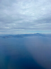 Aerial view of calm blue sea with scattered islands under a cloudy sky, showing the beauty of coastal landscapes and distant mountain ranges.