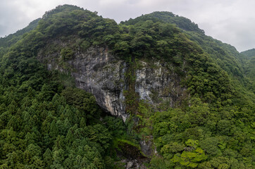 A dramatic, aerial view of a dark, rocky mountain covered in lush green vegetation. The scene evokes a sense of rugged beauty and isolation.
