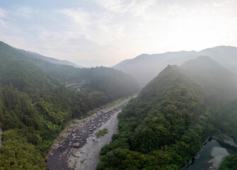 Aerial view of a lush, mountainous valley with a winding river and dense forest. Mist hangs in the air, creating a serene and atmospheric landscape.