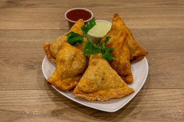 A plate of Indian samosas with tamarind and mint chutney isolated on a wooden table