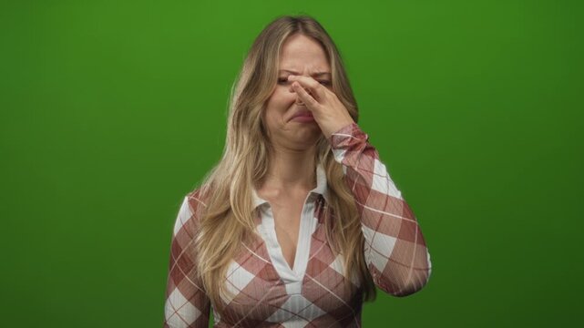 Woman pinches nose with fingers against a bright green studio backdrop showing a disgusted expression; disgust nausea.