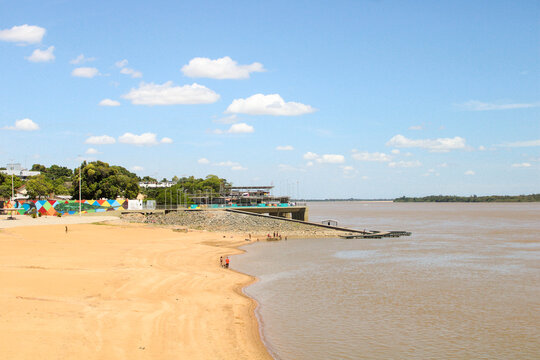 Vista ampla da paisagem de Roraima, mostrando o vasto rio de &aacute;guas turvas e a vegeta&ccedil;&atilde;o de savana (lavrado) que se estende at&eacute; o horizonte sob um c&eacute;u azul claro.