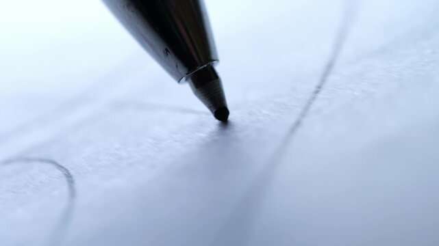 A close-up, low-angle shot of a silver ballpoint pen tip touching down on white paper ruled with a grid.
