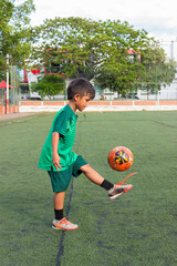 A young Colombian boy in a green uniform is playing with a ball on an artificial turf field in Neiva, Huila, Colombia. Concept of childhood and sports