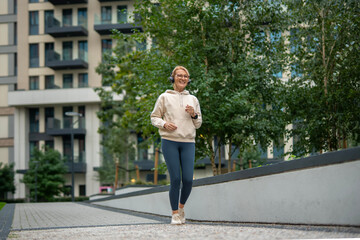 Fototapeta premium Mature woman jogging in urban park enjoying music