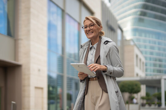 Senior business woman walking outdoors holding digital tablet
