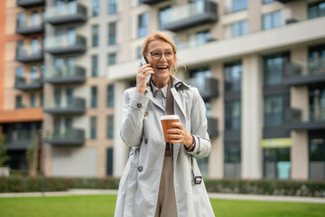 Mature woman laughing communicating on smartphone with coffee