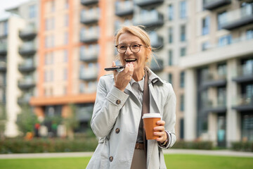 Mature woman using phone voice assistant and holding coffee