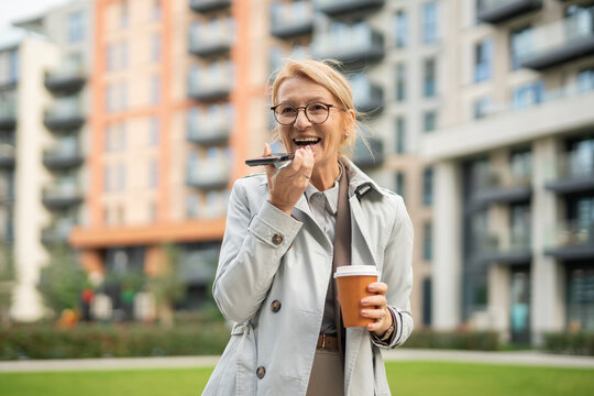 Mature woman using phone voice assistant and holding coffee