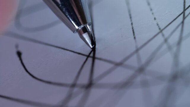 A close-up, low-angle shot of a silver ballpoint pen tip touching down on white paper ruled with a grid.
