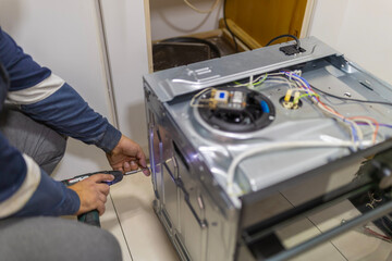Handyman repairing kitchen oven appliance during maintenance service