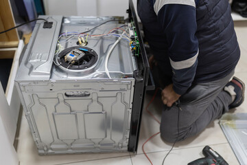 Technician repairing broken kitchen appliance with tools and wires