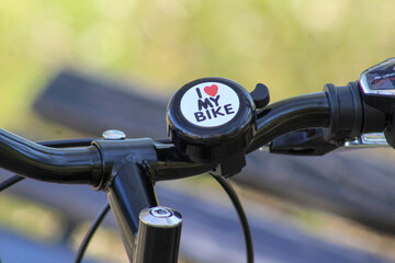 Close-up of a black bicycle handlebar with a bell that reads “I ♥ MY BIKE,” symbolizing passion for cycling and outdoor lifestyle.