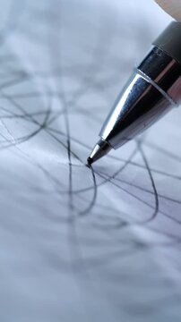 A vertical, extreme close-up of a metallic pen tip drawing intricate, chaotic lines on a piece of white paper.