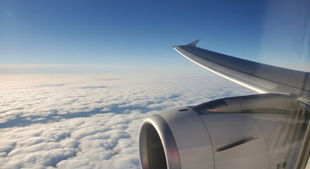 Airplane Window View. Airplane Wing and Engine Flying Above the Clouds and Blue Sky.
