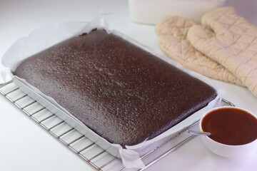 Freshly baked chocolate sheet cake in a parchment lined tray resting on a wire cooling rack