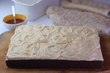 Chocolate sheet cake with a thick layer of buttercream frosting placed on a wooden cutting board