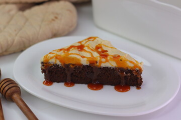Moist chocolate cake slice topped with buttercream frosting and drizzled with caramel cream sauce.