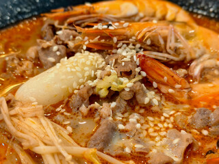 Shrimp, beef, and rice cake in spicy orange broth topped with sesame seeds
