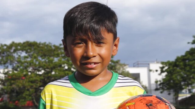 Portrait of a boy Colombian soccer player smiling and looking at the camera while holding a ball in his hands inside a sports club in Neiva, Huila, Colombia. Concept of childhood and happiness