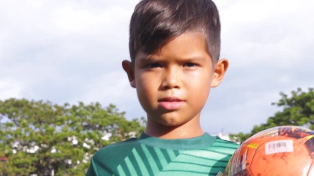 Portrait of a boy Hispanic soccer player smiling and looking at the camera while holding a ball in his hands inside a sports club in Neiva, Huila, Colombia. Concept of childhood and happiness