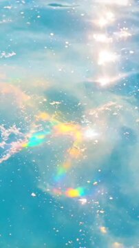 Soft shimmering light reflections on calm blue water surface with gentle rainbow highlights. seamless looping 4k video background