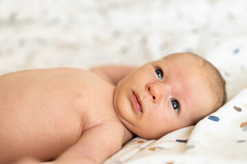 A newborn baby, lying on a soft, colorful blanket, gazes curiously at the viewer with wide eyes. The warm atmosphere highlights the baby's gentle features and innocence.