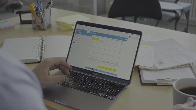 Busy hands typing on laptop displaying calendar application in an office