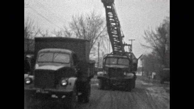 Old construction vehicles moving along city road, workers operating vintage machinery during repair process. Industrial retro atmosphere, sense of progress. Old film. Archival retro. Vintage archive.